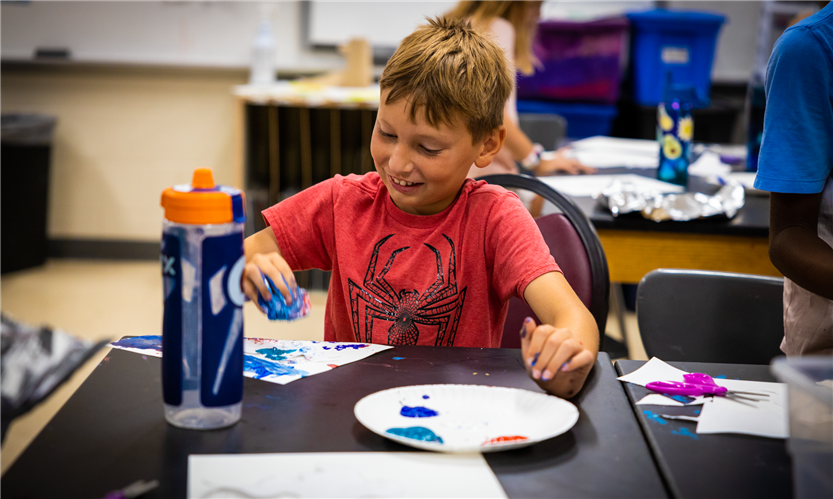 A boy wearing an orange shirt paints